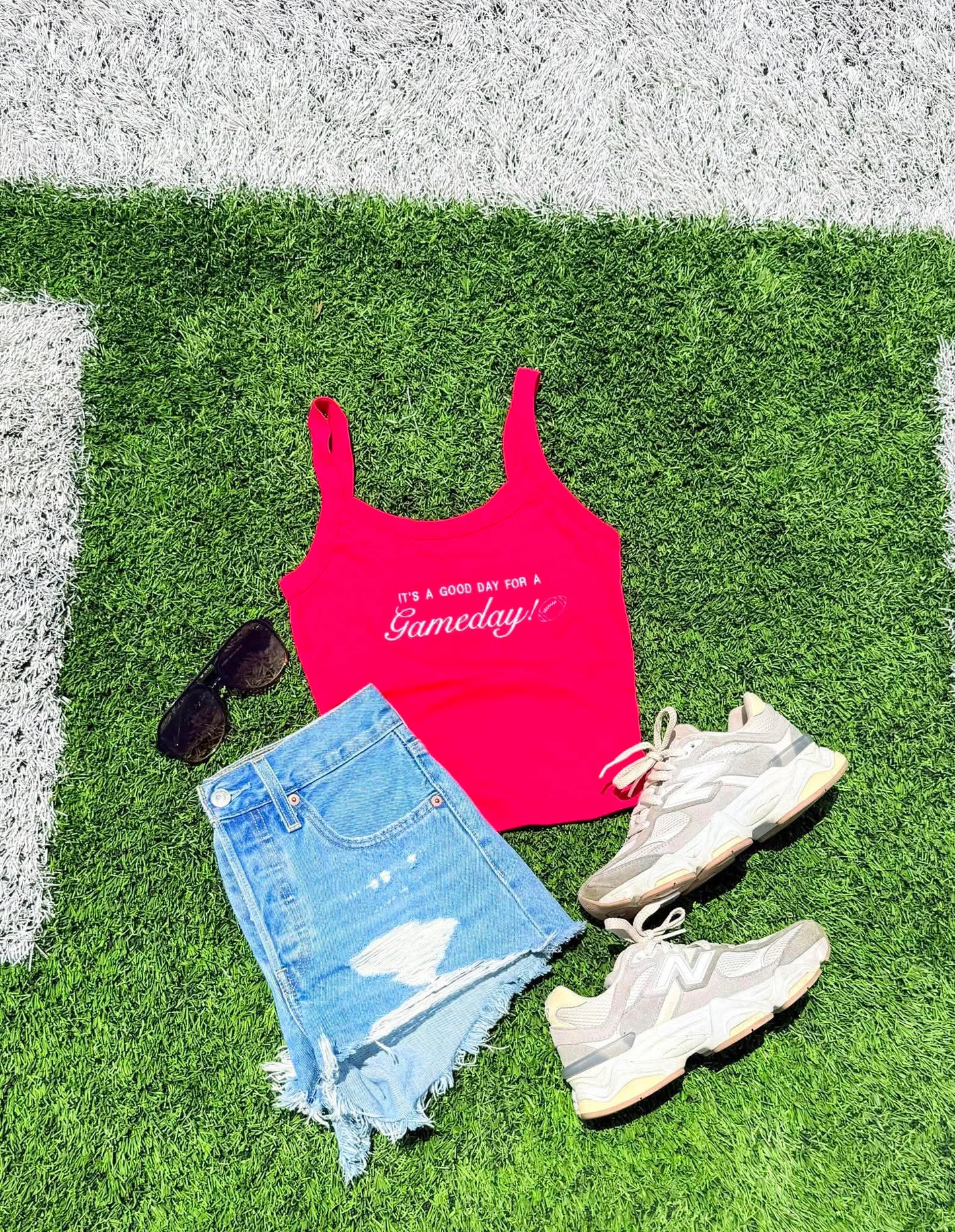Pink tank top with text, denim shorts, sneakers, and sunglasses on grass