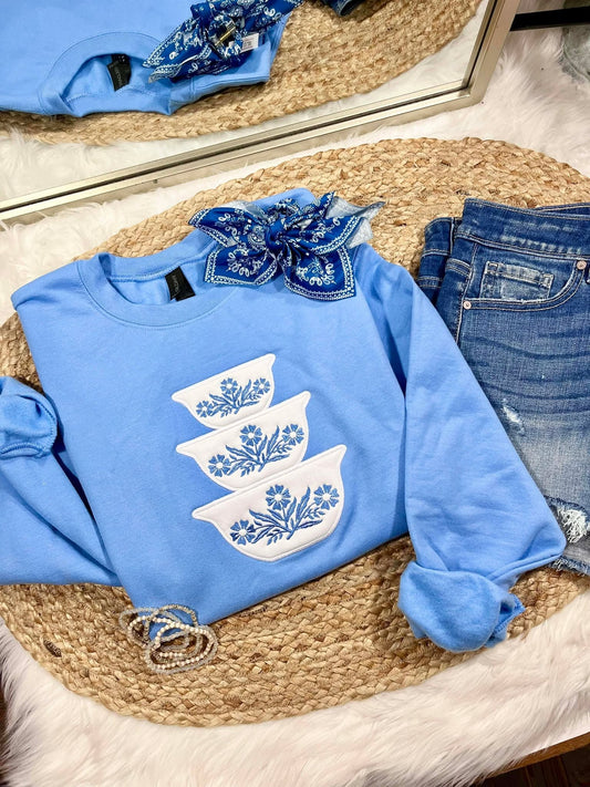 Blue sweatshirt with white floral designs on a woven mat