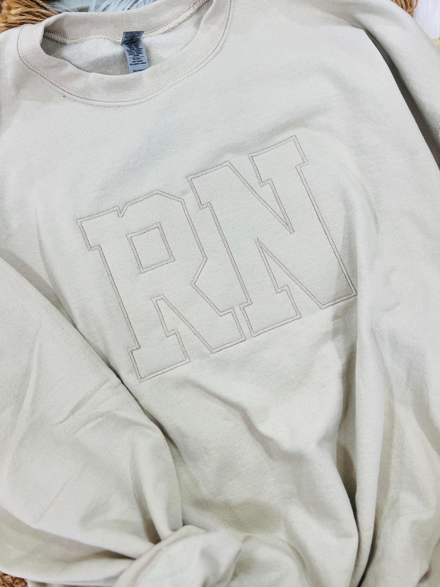 A beige embroidered sweatshirt with the letters 'RN' on the front.