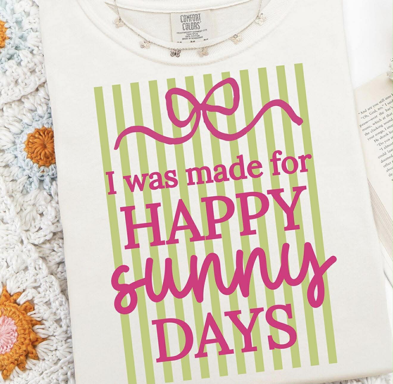 White shirt with green stripes and pink text 'I was made for HAPPY SUNNY DAYS' on a textured surface.