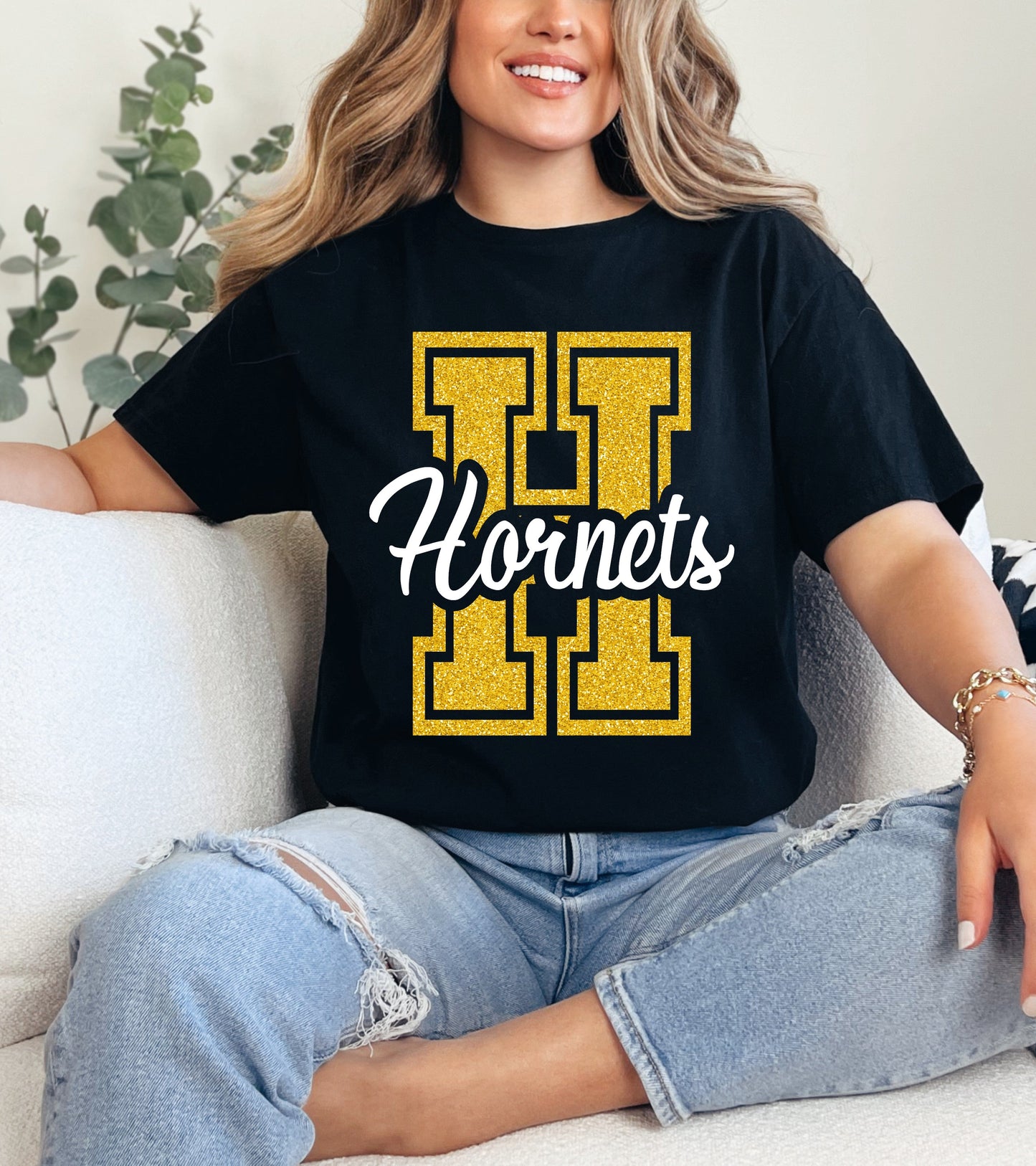 Person wearing a black t-shirt with 'Hornets' design, sitting on a couch.